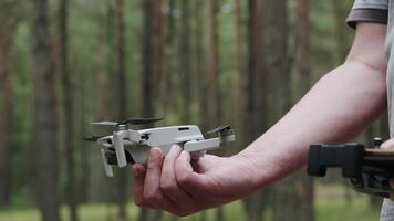 A quadcopter operator with a remote control holds the drone in front of him in focus outdoors. The drone takes off. video