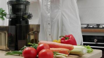 Person preparing fresh vegetables, including celery, tomatoes, and carrots, for juicing in a modern kitchen with a juicer. video