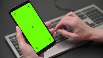 woman holding smartphone with green screen over keyboard. Hand typing text. video