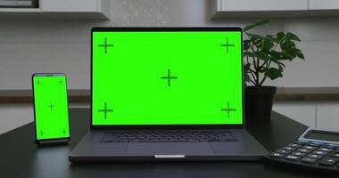 Laptop and smartphone with green screen on the table. Workplace mockup. video