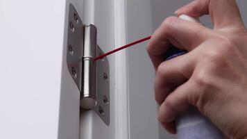 A man is oiling the door hinges. adjusting door hinge using lubricating oil. video