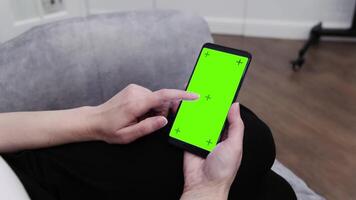a person sitting on a couch using a cell phone with a green screen. mobile app mockup. video