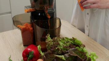Woman makes vegetable juice using a juicer in her home kitchen. Healthy detox vegetarian diet with cold pressed plant extractor to extract nutrients for smoothies. video