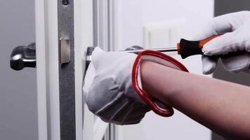 A handyman in white gloves repairs the lock on the door. close-up of a worker's hands installing a new door lock. video