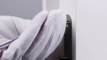 Handyman in white gloves repairs the lock on the door. close-up of a worker's hands installing a new door lock. video