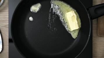 A butter pat melting on a black cast iron frying pan. Frying pan with melted butter on stove, close up. video