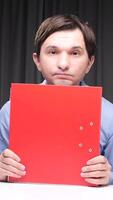 vertical Office worker hiding behind red folder at desk with laptop and binders video