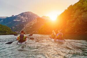A group of friends enjoying fun and kayaking exploring the calm river, surrounding forest and large natural river canyons during an idyllic sunset. photo