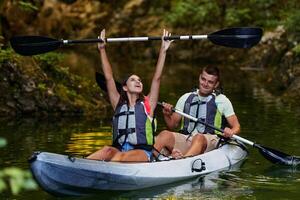 A young couple enjoying an idyllic kayak ride in the middle of a beautiful river surrounded by forest greenery photo