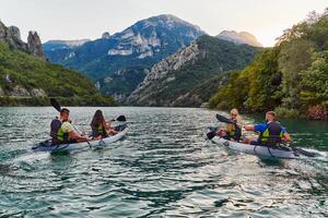 A group of friends enjoying fun and kayaking exploring the calm river, surrounding forest and large natural river canyons during an idyllic sunset. photo