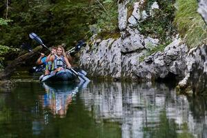 A young couple enjoying an idyllic kayak ride in the middle of a beautiful river surrounded by forest greenery photo