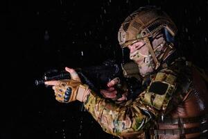 Army soldier in Combat Uniforms with an assault rifle, plate carrier and combat helmet going on a dangerous mission on a rainy night. photo