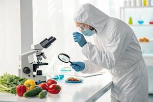 Biotechnology researcher examining fresh vegetables under microscope, showcasing intersection of science and food safety photo