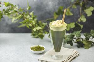 Glass of iced matcha latte with whipped cream and straw being decorated with ivy branches photo