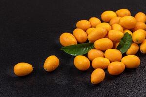 Fresh kumquats with leaves resting on wet black surface photo