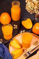 Two glasses and a carafe of persimmon juice are surrounded by fresh fruits and dried flowers, creating a vibrant and autumnal scene photo