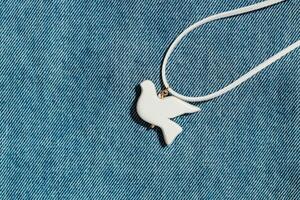 bijouterie white bird of polymer clay on the background of denim fabric photo