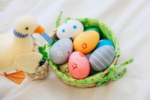 Colorful Easter eggs and a decorative duck on a soft white surface with a basket photo