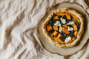 Vegetarian open pie with sweet potatoes, spinach, and goat cheese served on handmade ceramic plate in natural light photo