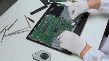 A technician in gloves works carefully on a laptop's motherboard, surrounded by tools and components in a tidy environment. Focus on precision and cleanliness is evident. video