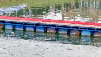 A floating bridge with a red surface rests on a tranquil body of water, symbolizing innovative transportation solutions photo