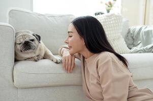 Woman Interacts Lovingly With a Sleeping Pug on a Cozy Living Room Sofa in Bright Sunlight photo