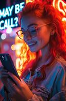 contento joven mujer con rojo pelo y lentes utilizando teléfono cerca neón firmar foto