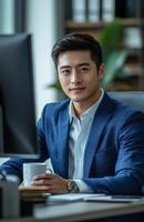 Young Asian businessman in blue suit working with computer and coffee mug in office photo