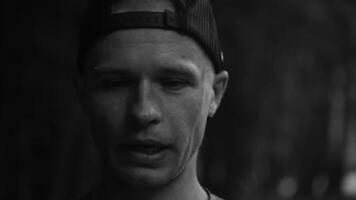 Portrait of mature man with sweat drops on his face after workout on blurred background. Sportsman in cap standing and wiping sweat from his face looking at camera close-up video