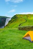 Cover page camping site with orange tent, and tourists in front of famous Skogafoss waterfall, while hiking in Iceland, summer, scenic view, with copy space photo