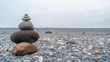 View of a pyramid made of stack of round stones put together at each other at stony gravel beach seacoast with copy space photo