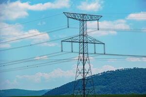 High voltage lines power pylons in a green landscape on a sunny day with clouds in the blue sky. photo