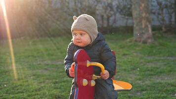 A cheerful toddler joyfully plays on colorful playground equipment, wearing a cozy hat and warm jacket, enjoying a delightful day outdoors in the bright sunlight video