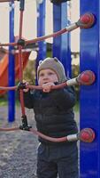 A happy toddler plays on a colorful climbing frame at the playground, surrounded by vibrant structures and beautiful sunlight. A delightful moment of childhood exploration. video