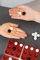 Children's hands place black and white marbles on the game board. The players focus on their next move, strategizing with each piece to win the game. photo