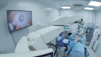 Surgeon looking into the microscope at the eye of female patient at the operating room. Doctor using microscope during eye surgery process, treatment of cataract and diopter correction. 16 video