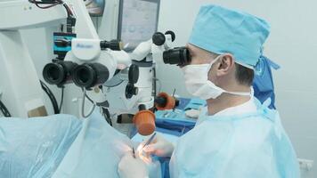 Surgeon looking into the microscope at the eye of female patient at the operating room. Doctor using microscope during eye surgery process, treatment of cataract and diopter correction. 13 video
