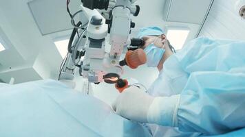 Surgeon looking into the microscope at the eye of female patient at the operating room. Doctor using microscope during eye surgery process, treatment of cataract and diopter correction. 11 video