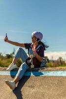 Latin skater taking selfie and calling with smartphone in pump track photo