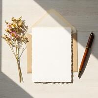 Soft, vintage-inspired flat lay with blank paper, a brown envelope, a wooden fountain pen, and a delicate bouquet of dried flowers on a light wood surface, ideal for letters and invitations. photo