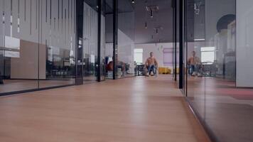 Modern startup coworking office corridor with glass walls, featuring a man with disabilities in a wheelchair. The space showcases an inclusive, accessible workplace with a sleek, open design and video
