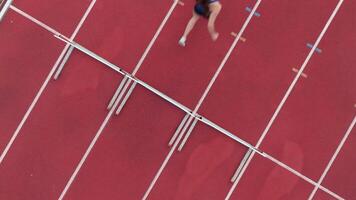 Top down view aerial drone shot of a professional female athlete sprinting on a large stadium athletics track. Dynamic slow motion cinematic footage captures her power, speed, and determination in video