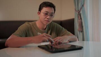 Focused on the task a young man with glasses concentrates intently on writing notes, his stylus poised over a tablet, showcasing a dedicated and determined approach to work or study. video