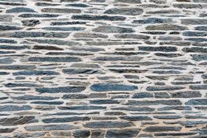 Flat dark grey blue stones laid between a thick layer of cement create a solid wall, creating a unique pattern that adds depth and texture to the background, photo