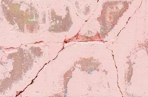 Close-up of a cracked pink stucco wall showing layers of other colors underneath,signs of erosion and deterioration creating an abstract textured background, photo
