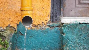 Water flowing from a yellow pipe against colorful wall in urban area video
