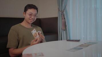 Counting finances a young man carefully counts money at a table, a thoughtful expression on his face. This photo captures a moment of financial management, representing budgeting, saving. video