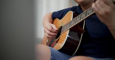 Handheld selective focus shot, Asian man sitting on sofa enjoying playing music with guitar and looking at music chords on laptop in living room with relaxation. video