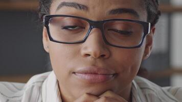 African American woman with glasses contemplates while teaching online, feeling bored. She is a remote educator dedicated to guiding students in their learning journey from her workspace. video