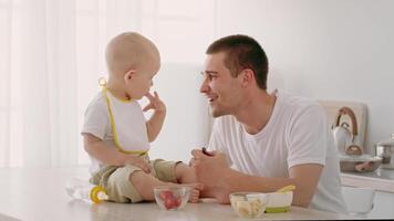 A playful toddler in a bib sits on a countertop, curiously looking at a caregiver. The caregiver engages with the child, creating a warm and nurturing atmosphere during snack time. video
